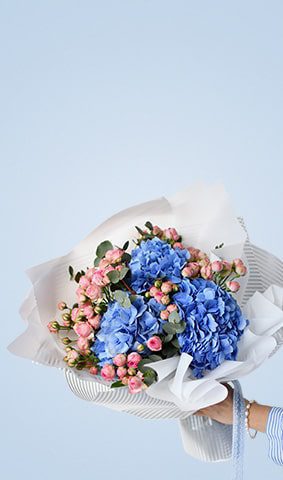 Elegant bouquet featuring blue hydrangeas and delicate pink buds wrapped in white paper.