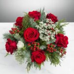 A bouquet of red roses with greenery in a clear glass vase..