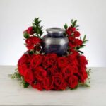 A silver urn surrounded by a heart-shaped arrangement of red roses.
