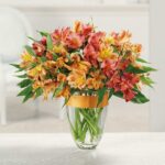 Vibrant bouquet of orange, yellow, and red flowers in a clear glass vase.