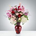 Elegant bouquet of pink lilies, red roses, and white hydrangeas in a red vase.