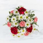 A bouquet of red roses, white daisies, and pink carnations.