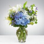 Elegant bouquet with blue hydrangeas and white lilies in a clear glass vase.