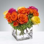 Vibrant bouquet of assorted roses in a clear square vase.