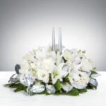 Elegant white floral arrangement with silver accents and candles.