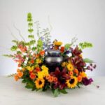 A black urn surrounded by a vibrant floral arrangement.