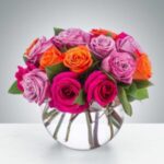 A vibrant bouquet of roses in a round glass vase.