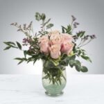 A bouquet of pink roses and greenery in a clear glass vase.