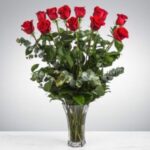 A bouquet of vibrant red roses in a clear glass vase against a plain background.