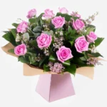 A bouquet of pink roses with green leaves wrapped in pink paper.