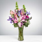 Elegant bouquet of pink lilies and purple flowers in a clear glass vase.