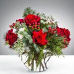A bouquet of red roses with greenery in a clear glass vase.