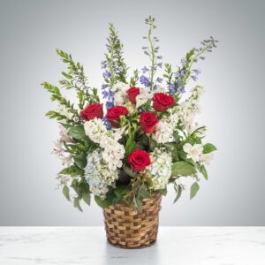 Elegant floral arrangement with red roses and mixed flowers in a woven basket.