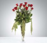 Elegant bouquet of red roses with cascading greenery in a clear glass vase.