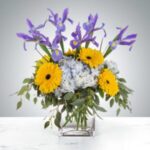 A vibrant bouquet with yellow sunflowers and purple irises in a clear glass vase.