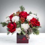 Festive floral arrangement with red roses and white chrysanthemums in a red vase.