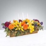Bright floral centerpiece with orange lilies and yellow flowers in a wooden container.