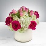 Elegant bouquet of pink and red roses with white hydrangeas in a white vase.