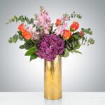 Elegant bouquet of mixed flowers in a tall gold vase.