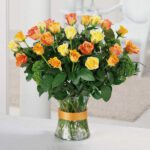 A vibrant bouquet of yellow and orange roses in a glass vase.