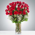 A bouquet of red roses with baby's breath in a clear glass vase.