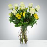 Elegant bouquet of white roses and yellow flowers in a clear glass vase.