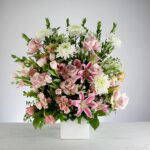 Elegant floral arrangement with pink lilies and white flowers in a white vase.
