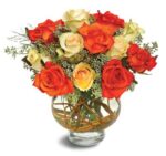 Vibrant bouquet of orange and cream roses in a clear glass vase.
