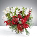 Festive bouquet with white flowers, red berries, and decorative mesh in a glass vase.