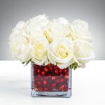 White roses in a clear vase with red beads.