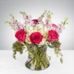 A vibrant bouquet with pink roses and delicate flowers in a clear vase.