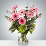 Bright pink gerbera daisies in a clear glass vase with green foliage.