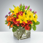 Bright bouquet of yellow lilies and orange flowers in a square glass vase.
