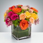 Vibrant mixed rose bouquet in a modern square glass vase.