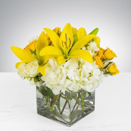 Bright yellow lilies and white flowers in a square glass vase.