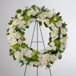 A white floral wreath on a stand against a plain background.