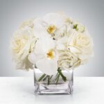 Elegant white flower arrangement in a clear square vase.