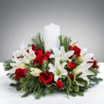 Elegant floral centerpiece with red roses, white lilies, and a tall white candle.