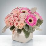 A delicate bouquet of pink roses and gerbera daisies in a white vase.
