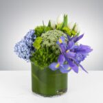 Elegant floral arrangement in a clear vase with green leaves and vibrant purple and blue flowers.