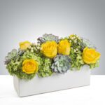Yellow roses and succulents in a white rectangular vase.