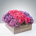 A wooden box filled with pink roses and purple hydrangeas.