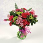 Vibrant mixed flower bouquet in a clear vase with pink ribbon.