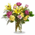 A vibrant bouquet of yellow lilies and pink roses in a clear glass vase.