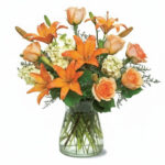 A vibrant bouquet of orange lilies and roses in a clear glass vase.
