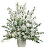 A tall, elegant all-white floral arrangement in a neutral ribbed ceramic pot, featuring gladiolus, spider mums, and carnations with lush green foliage.