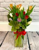 Elegant bouquet with tulips and greenery in a clear vase tied with a red ribbon.