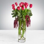 Elegant bouquet of pink tulips and hanging greenery in a clear glass vase.