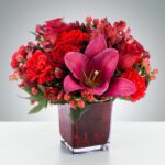 Vibrant red and pink floral arrangement in a square glass vase.