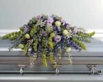 A casket adorned with a large, elegant floral arrangement in soft pastel colors.